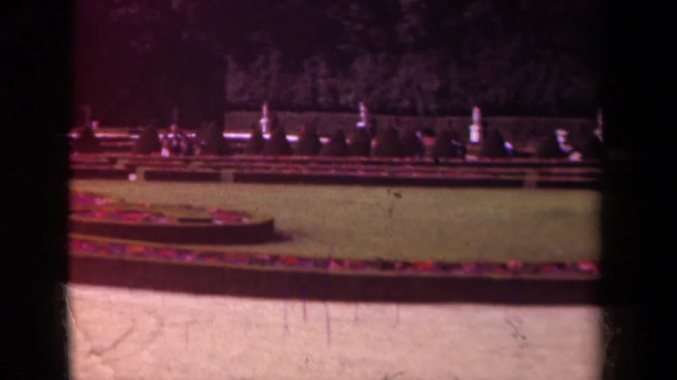 1939 Paris frame of manicured grounds with circular planting beds, lawn, low hedges, and dark trees in soft 8mm color.
