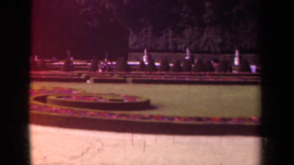 1939 Paris home-movie view of formal garden landscaping, including a circular bed, clipped lawn, hedges, and shaded trees.