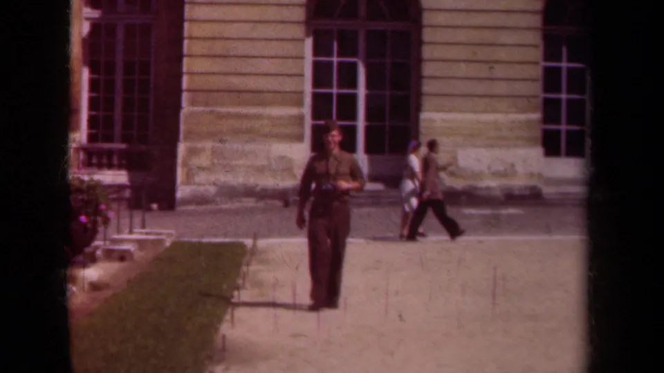 In 1939 Paris home-movie footage, a uniformed man walks toward the camera near a large stone building as pedestrians pass behind him.