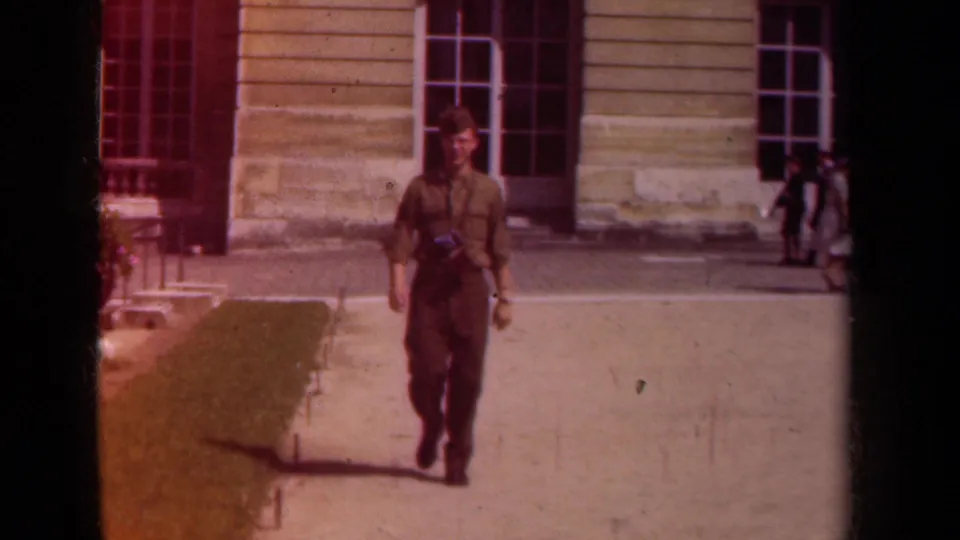 Near the end of the 1939 Paris clip, the uniformed man stands close in frame while the grand building facade remains visible behind him.