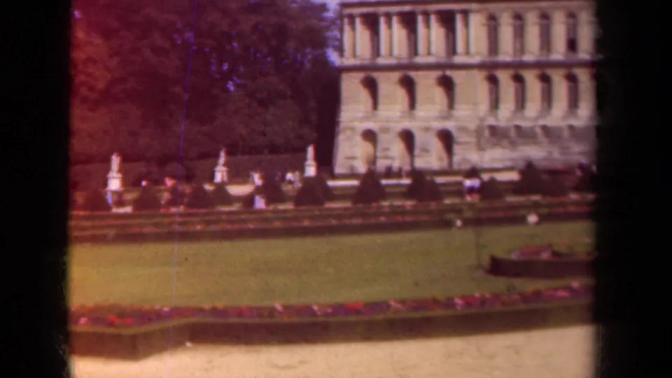 A 1939 Paris garden view shows lawns, flowerbeds, hedges, small visitor figures, and more of the large arched historic building.