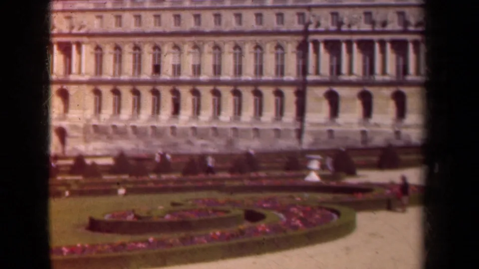1939 Paris garden view with flowerbeds, trimmed lawn, ornate architecture, and distant visitors.