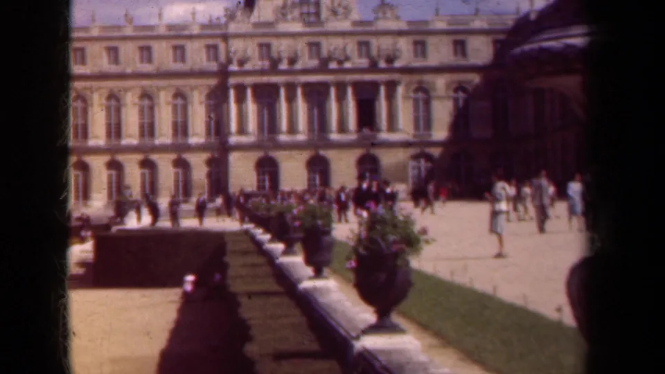 1939 Paris home-movie frame of visitors crossing palace gardens beside urn planters and hedges.