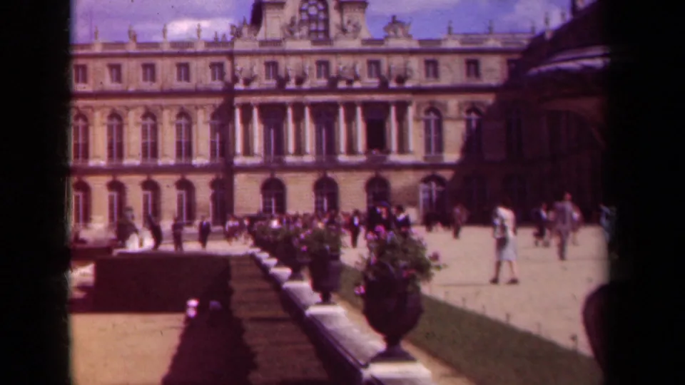 1939 Paris garden scene with tourists, decorative vases, formal hedges, and palace architecture.