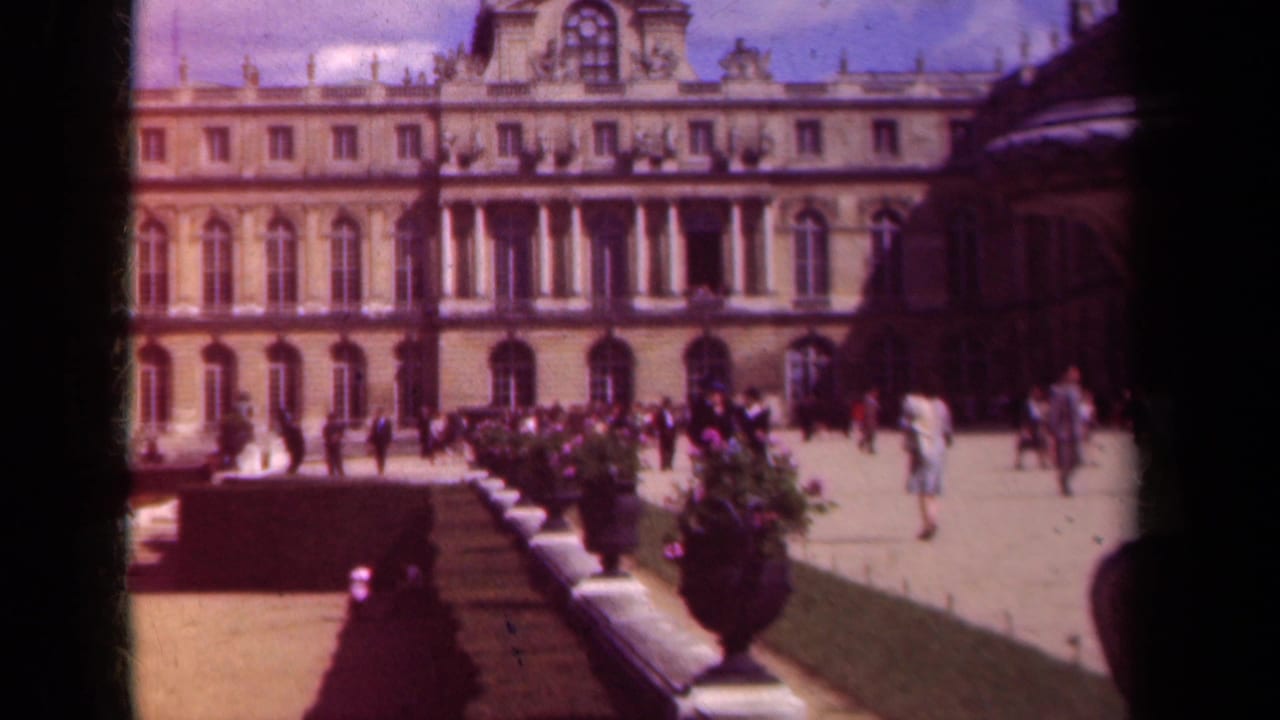 Grand historic facade beside formal garden beds with visitors walking in the courtyard.