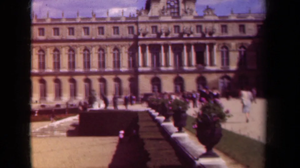 1939 Paris 8mm still showing a long historic facade, garden urns, hedges, and small groups of visitors in the courtyard.