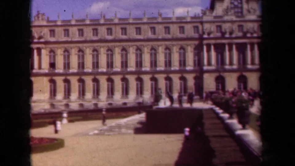 Paris-area palace exterior on 8mm film, showing the long facade, formal courtyard, garden borders, and visitors near the entrance area.