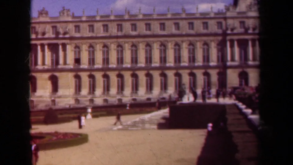 A soft 8mm view of a formal palace courtyard in France, with the facade filling the frame and visitors moving across the open space.