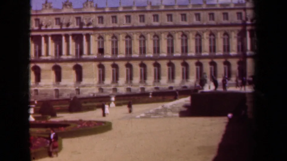 Wide 1939 home-movie frame of a Paris-area palace courtyard, showing classical architecture, formal plantings, and visitors at a distance.