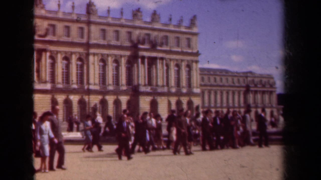 1939 Paris travel footage shows a group of tourists crossing a broad courtyard in front of a grand classical palace facade.
