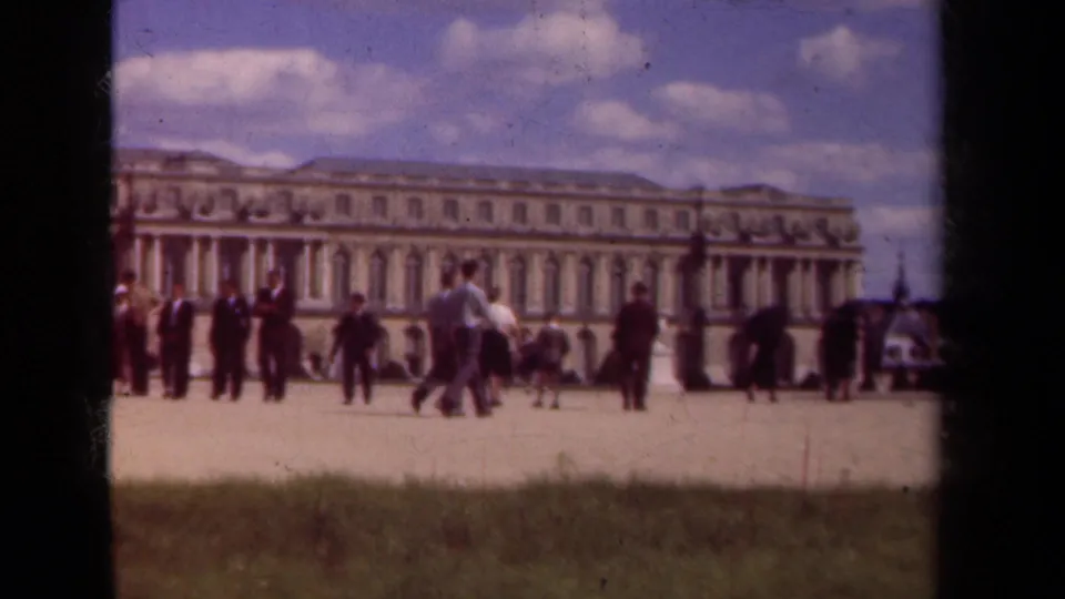 A wider 1939 Paris courtyard view shows scattered tourists crossing in front of a long classical palace facade and a foreground lawn.