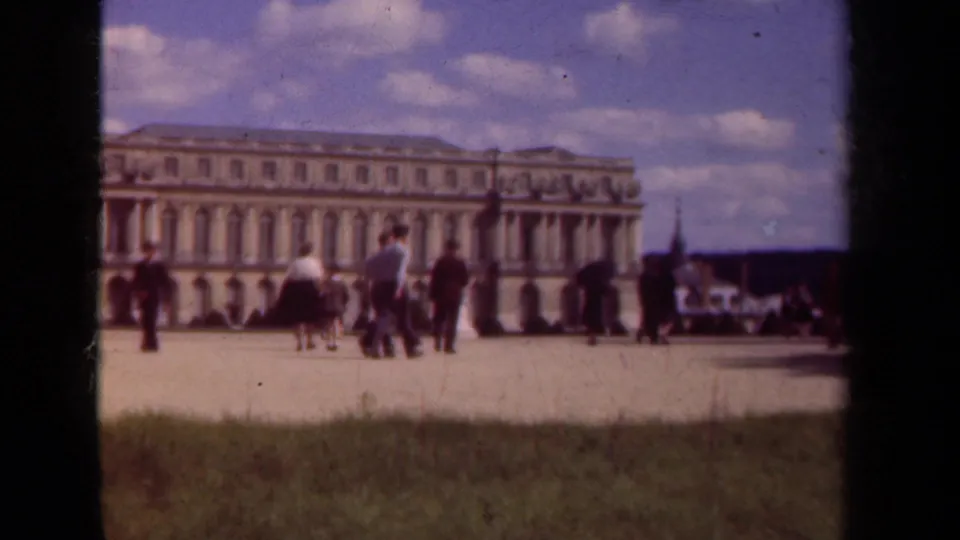Tourists in period dress move through the courtyard in front of a grand Paris-area palace facade in 1939 footage.