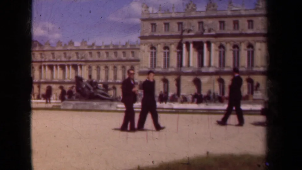 A 1939 home-movie frame shows suited visitors walking past ornate palace buildings in the Paris area.