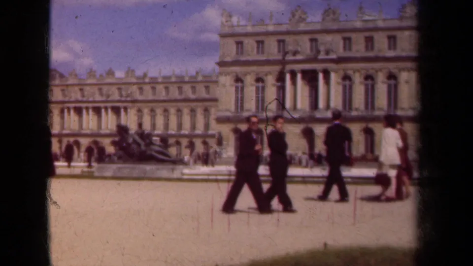 Tourists walk across the palace courtyard in 1939 Paris-area travel footage, including a woman in a light dress at right.