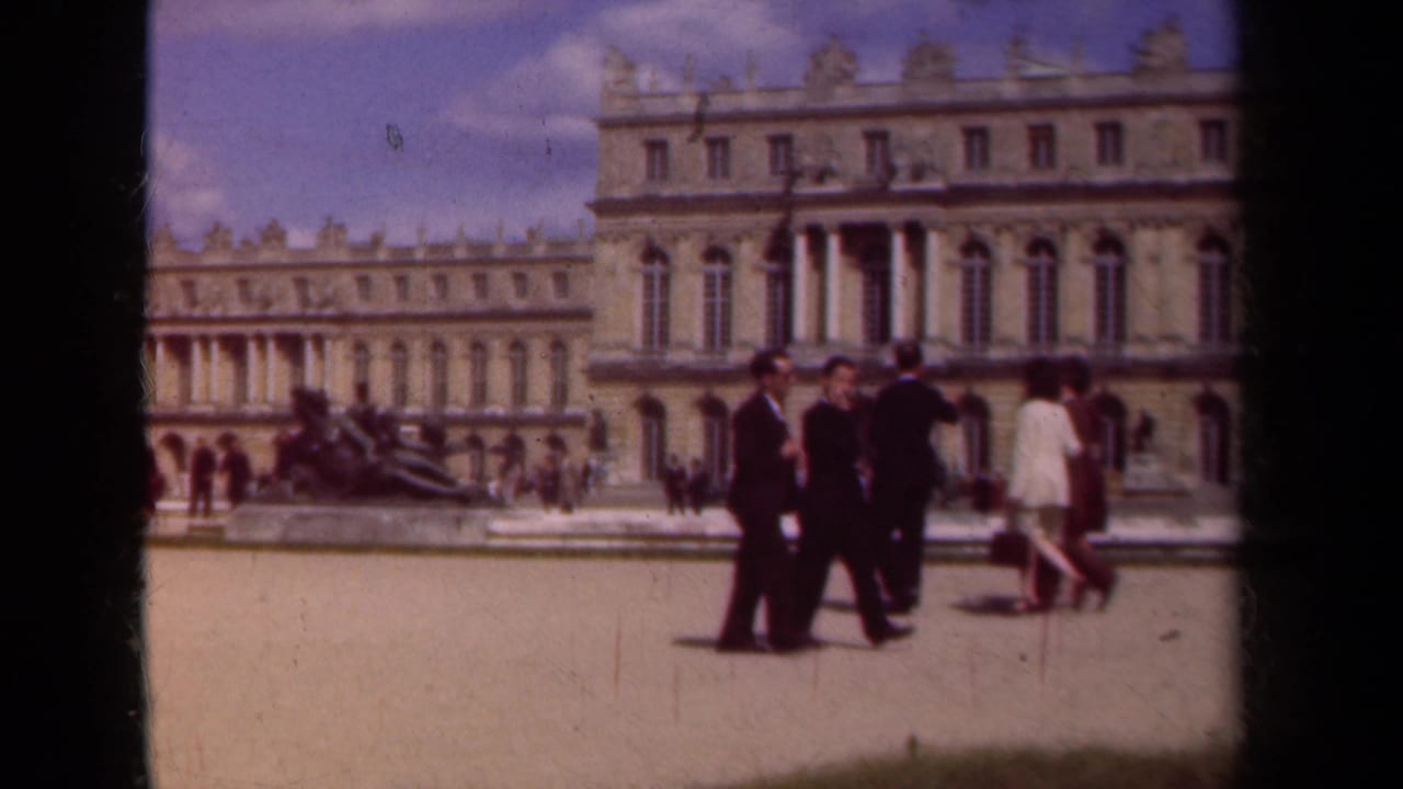 1939 8mm view of adults in suits and light clothing crossing a sunlit palace courtyard in Paris, France.
