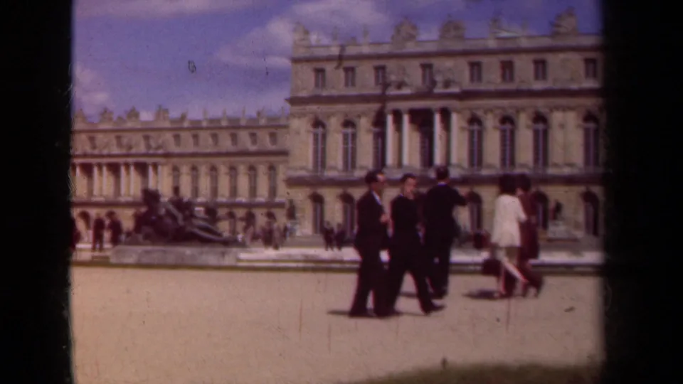 1939 8mm view of adults in suits and light clothing crossing a sunlit palace courtyard in Paris, France.