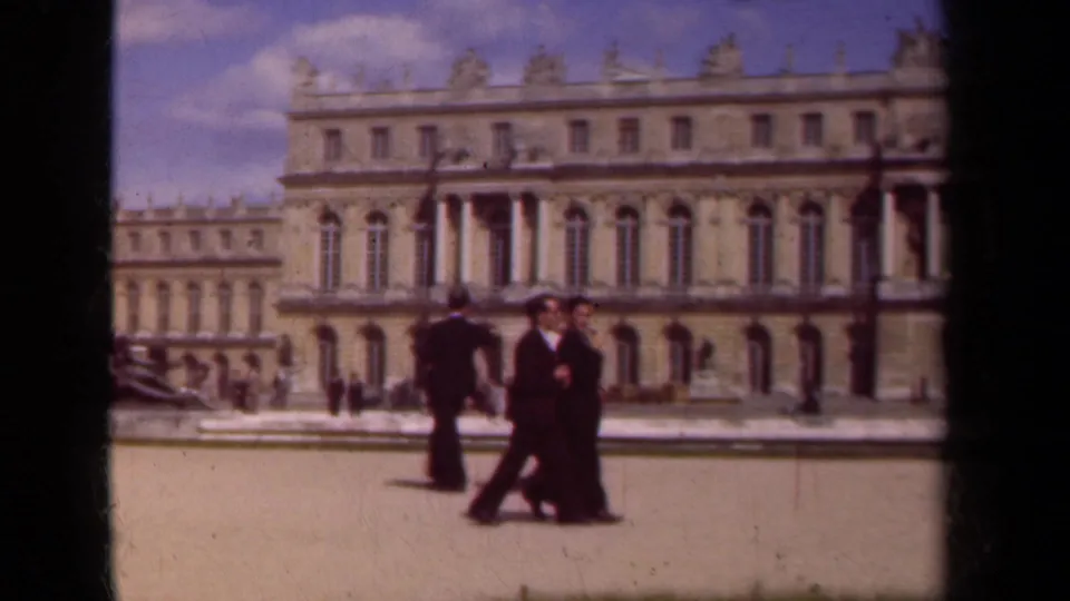 Adults pass through the palace courtyard, with a formal stone facade and roofline sculpture behind them in Paris, France.