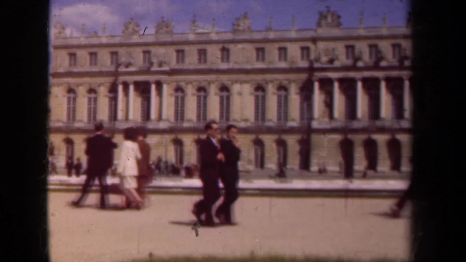 A woman in a light outfit and several suited adults cross the palace courtyard in this 1939 Paris home-movie frame.
