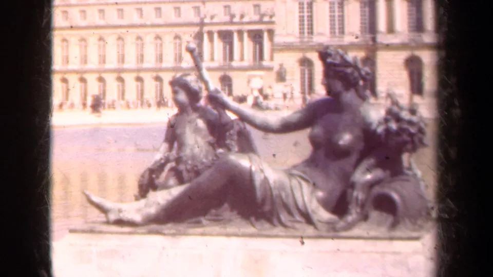 Close 1939 travel-film view of a reclining classical figure group in front of palace architecture and a bright reflecting pool.