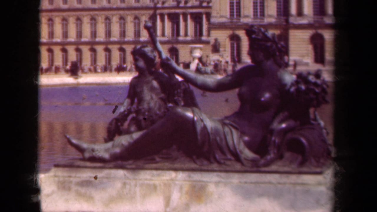 1939 8mm Versailles garden view of a bronze reclining female figure with a child figure, fountain water, and palace facade beyond.