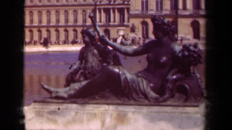 1939 8mm Versailles garden view of a bronze reclining female figure with a child figure, fountain water, and palace facade beyond.