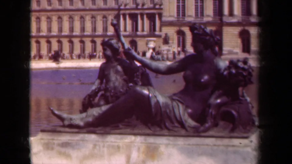 A visitor-shot 1939 Versailles frame shows the reclining bronze sculpture, water basin, stone edge, and palace architecture in soft color.