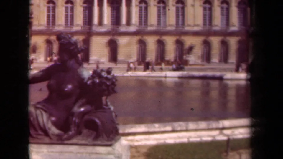 Late frame from the 1939 Versailles clip shows the bronze sculpture partly cropped at left, with fountain water, stonework, and the palace facade behind.