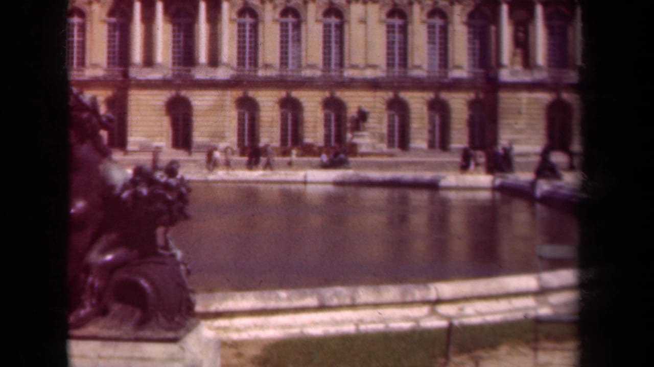 Formal pool and palace facade with visitors walking along the water edge.