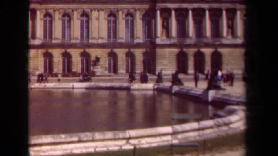 Wide 8mm view across a formal Paris pool toward a palace facade, with visitors strolling and pausing along the walkway.
