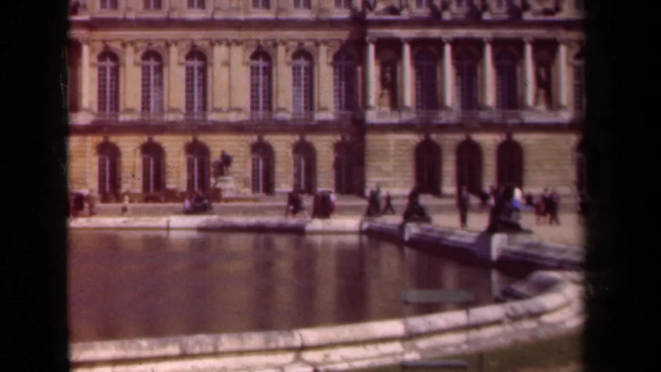 Soft-focus 1939 Paris frame with a reflecting pool, classical facade, and distant visitors near the water's edge.