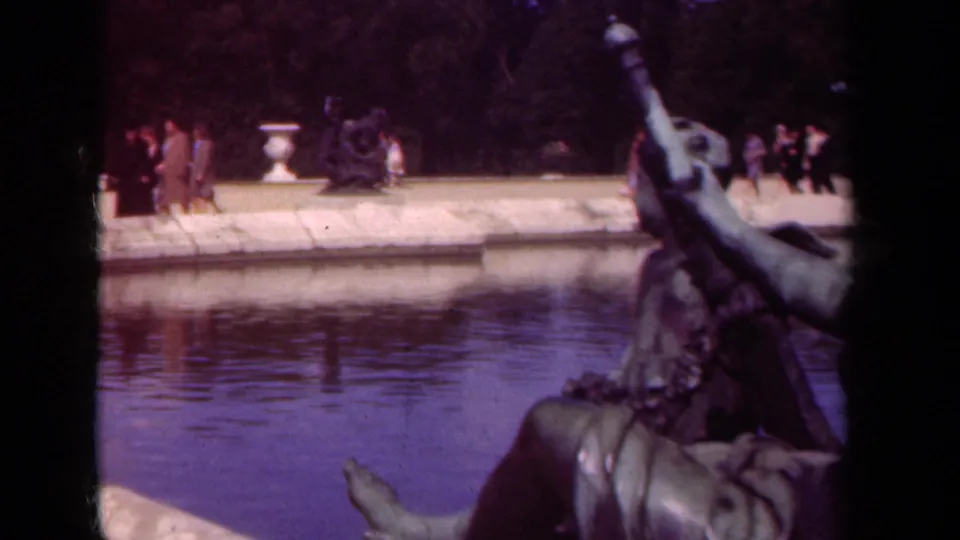 1939 Paris home-movie frame with a bronze figure in the foreground and visitors moving along the far side of the pond.
