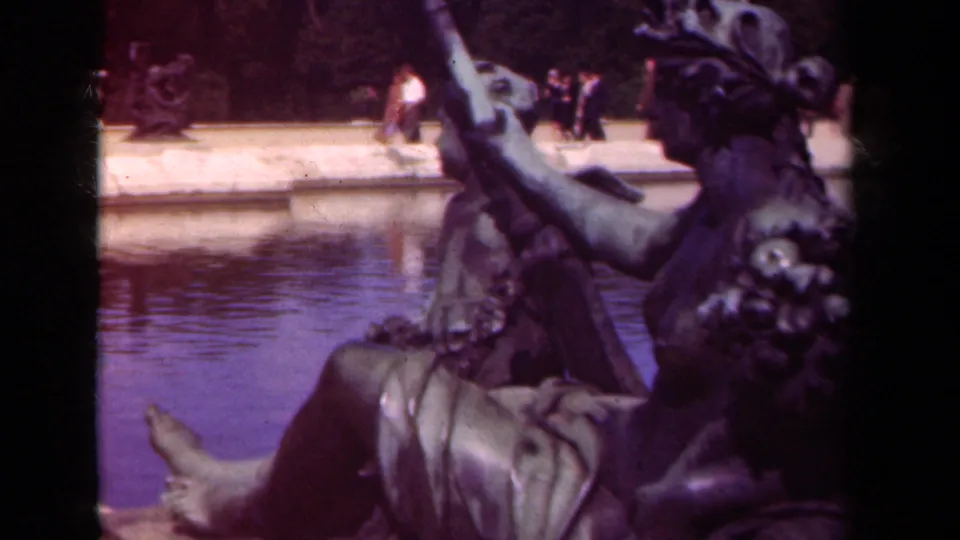 1939 Paris park frame with close bronze statuary, rippling pond reflections, and pedestrians on the far stone path.