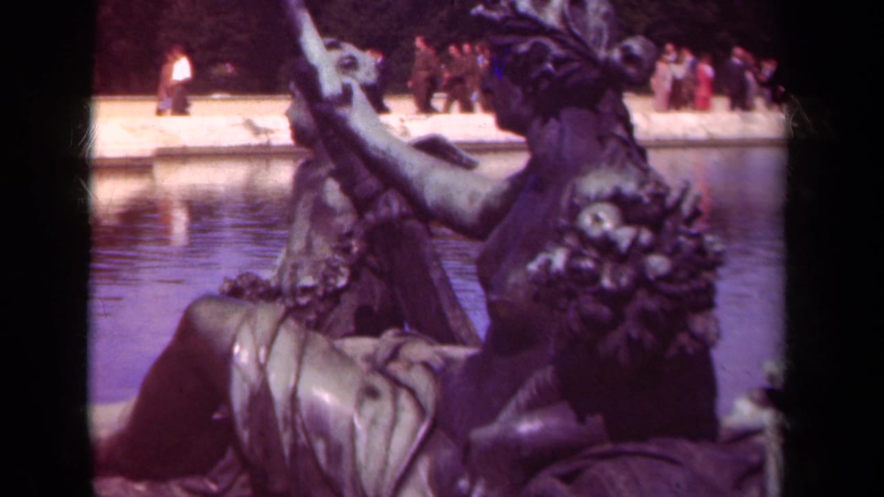 Close 8mm view of bronze statuary in a Paris formal garden, with a pool and distant visitors visible behind it.