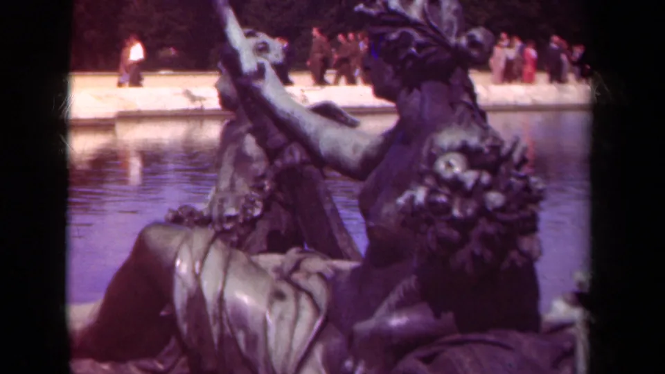 Close 8mm view of bronze statuary in a Paris formal garden, with a pool and distant visitors visible behind it.