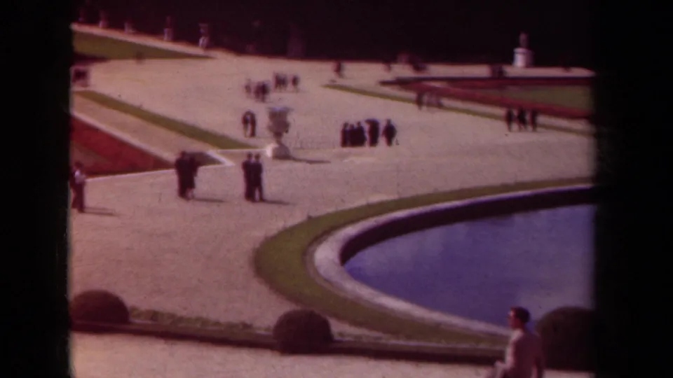 1939 Paris garden view with visitors on broad gravel paths, a curved pool edge, clipped grass, and red flowerbeds.