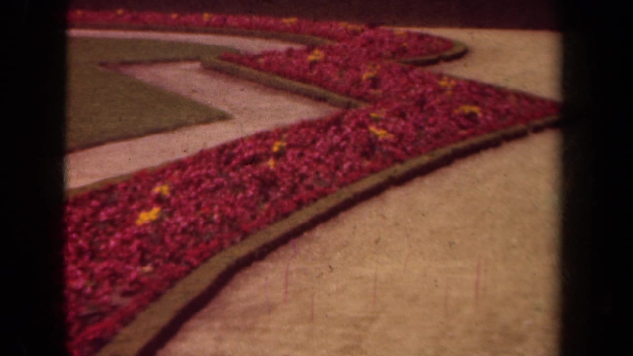 Curving red flower border beside pale walkways and a manicured lawn.