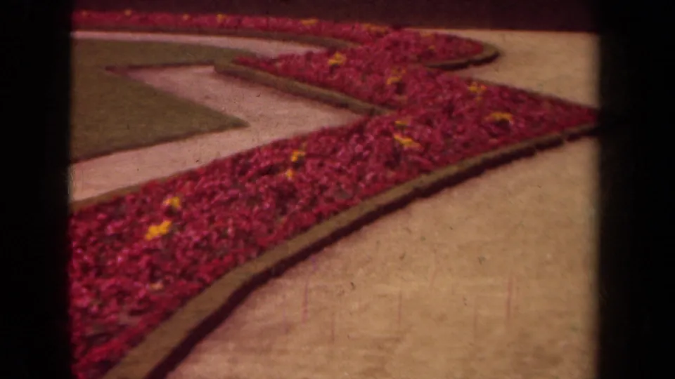 1939 Paris home-movie frame showing a sweeping red flower border with yellow accents beside paths and clipped grass.