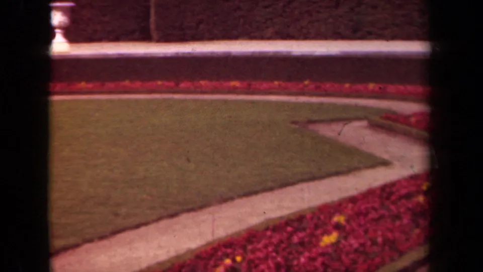 1939 Paris home-movie still showing a pale path, green lawn, and red flower border with yellow accents.