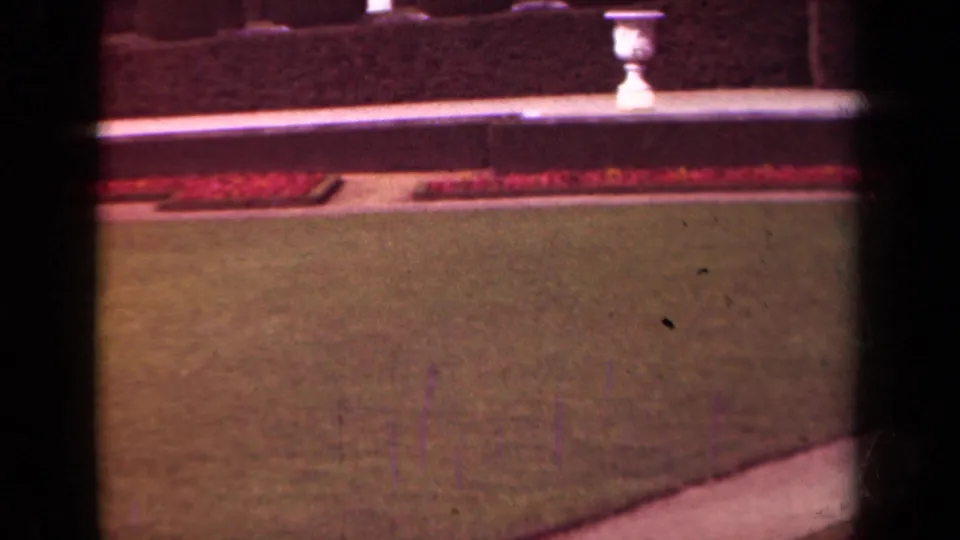 1939 Paris garden frame with soft focus, broad lawn, red flowerbeds, low stone wall, hedge, white urns, and dark gate edges.