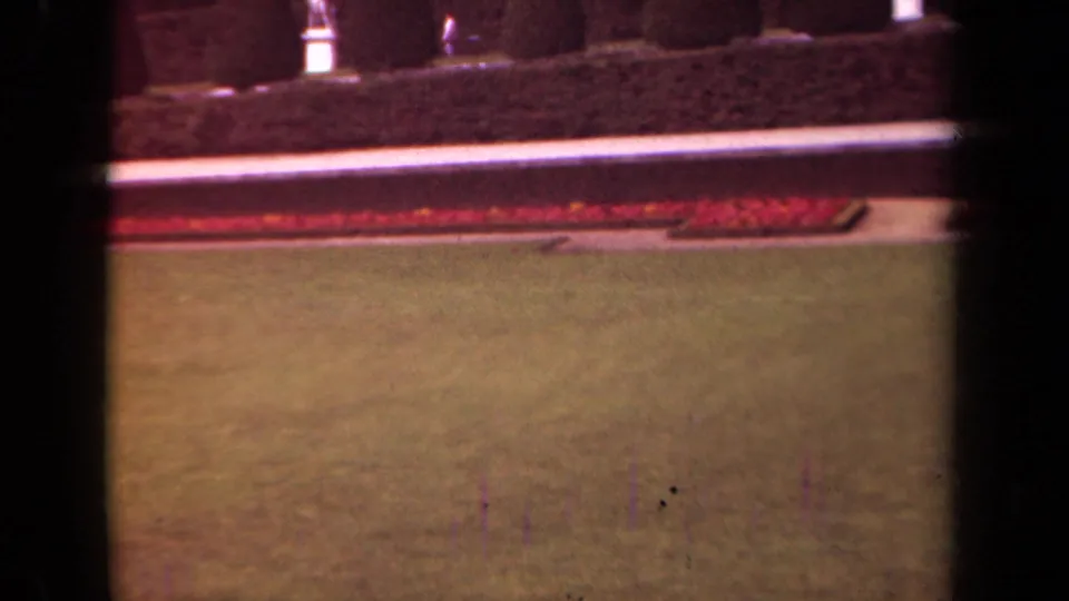 1939 Paris garden view with lawn, red flower beds, pale walkway, clipped hedge, and heavy film-frame edge from the 8mm scan.