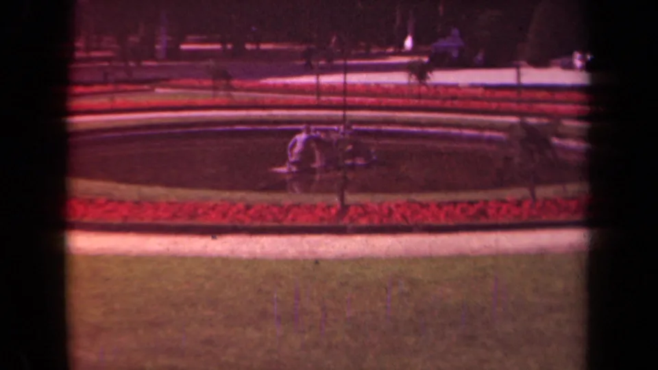 1939 Paris garden frame with a circular fountain, red flower beds, paths, lawn, and small distant visitors near the water feature.