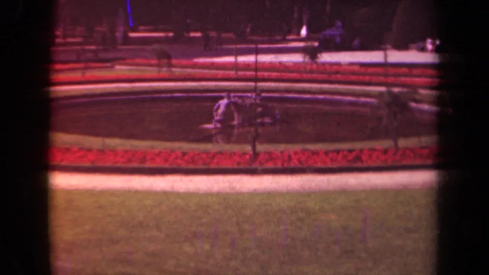 Warm-toned 1939 Paris frame showing red flowerbeds, a pale path, grass, railings, and a circular zoo attraction beyond.