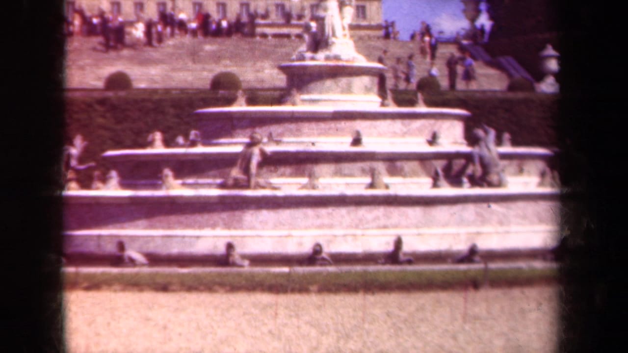 Multi-tiered fountain with statues, visitors on terrace steps, and dark film borders.