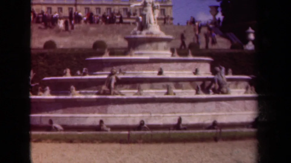 1939 Paris home-movie view of the fountain basin and statues with distant visitors along the terrace and a garden strip below.