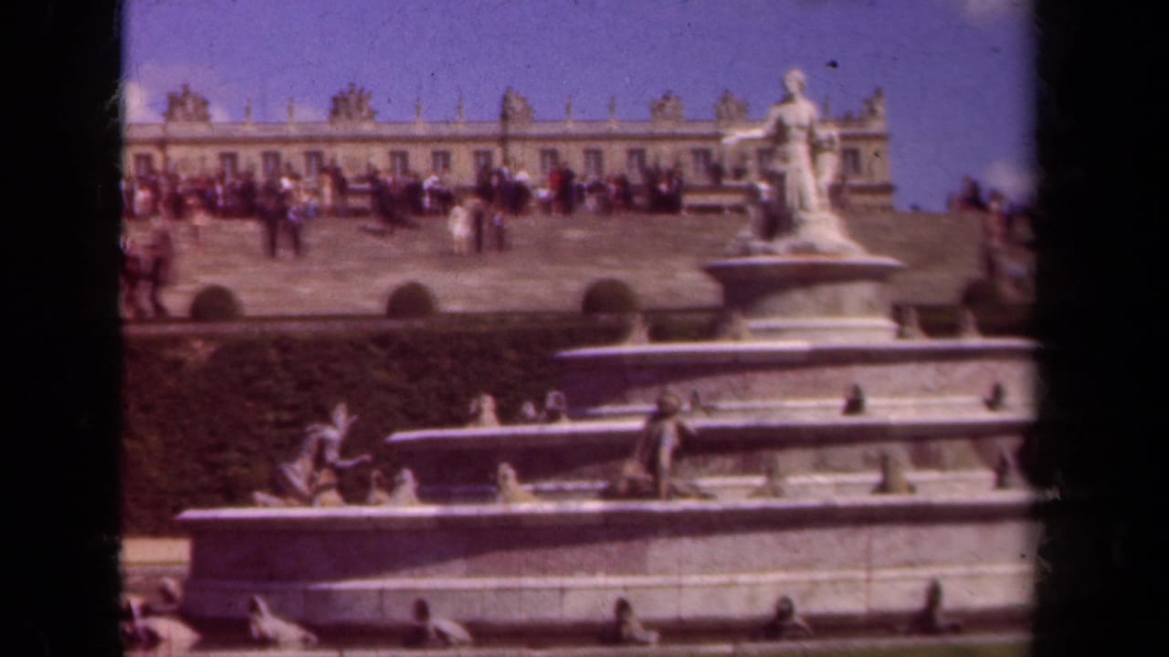 Tourists on a palace terrace above a large stone fountain with statues.