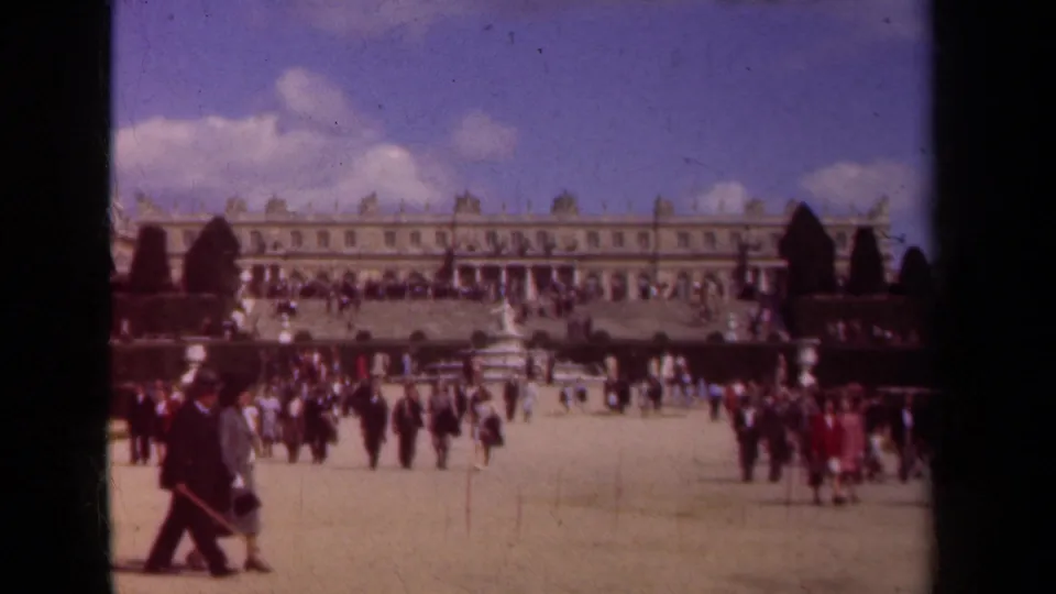 1939 Paris home-movie frame showing visitors crossing open palace grounds before a long formal facade and garden features.
