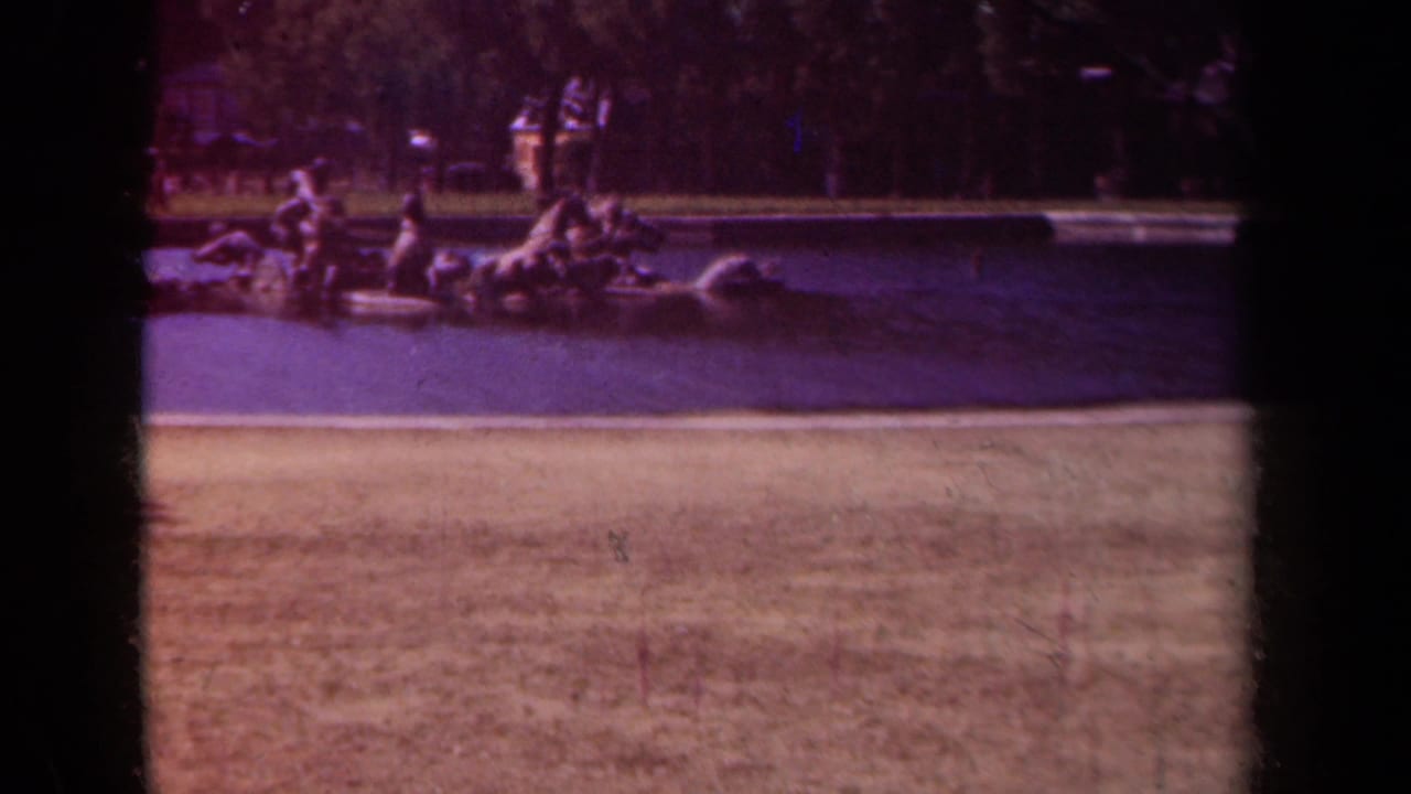Ornamental horse sculpture in a fountain basin with trees and distant visitors behind it.