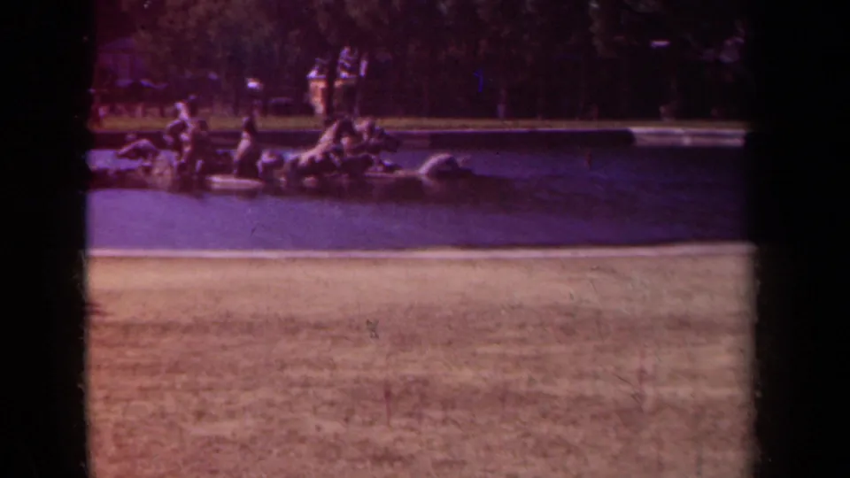 1939 Paris home-movie frame showing a horse-and-figure fountain sculpture across a broad water basin, with trees and park visitors in the background.
