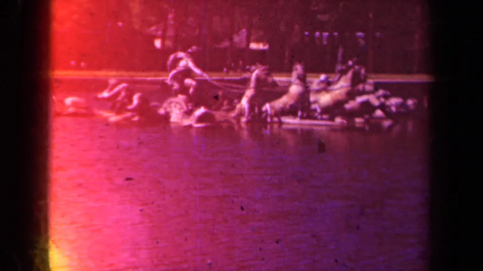 1939 8mm Paris garden view with a distant ornamental fountain or sculpture, water, trees, and strong red exposure flare.