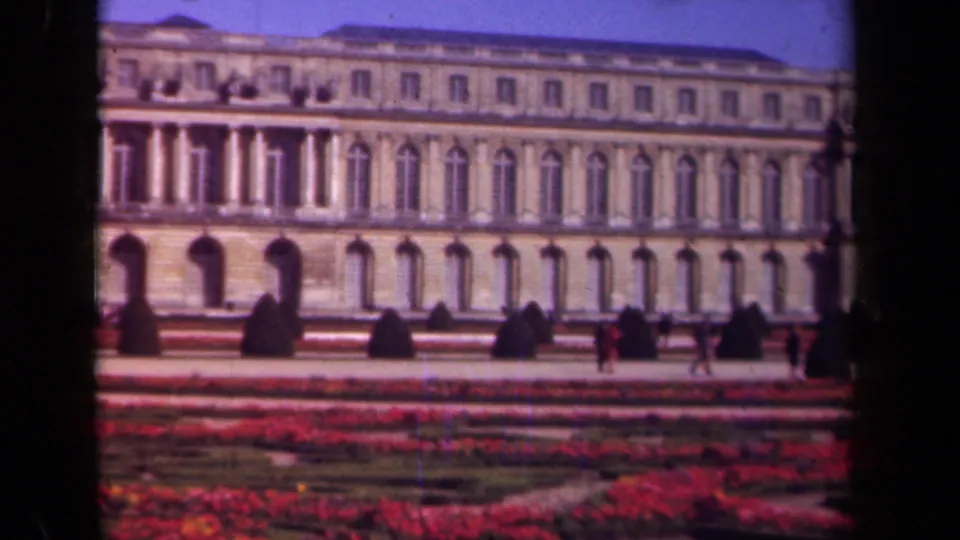 1939 Paris frame showing the building more prominently above formal red flower beds, trimmed greenery, and distant visitors on the path.